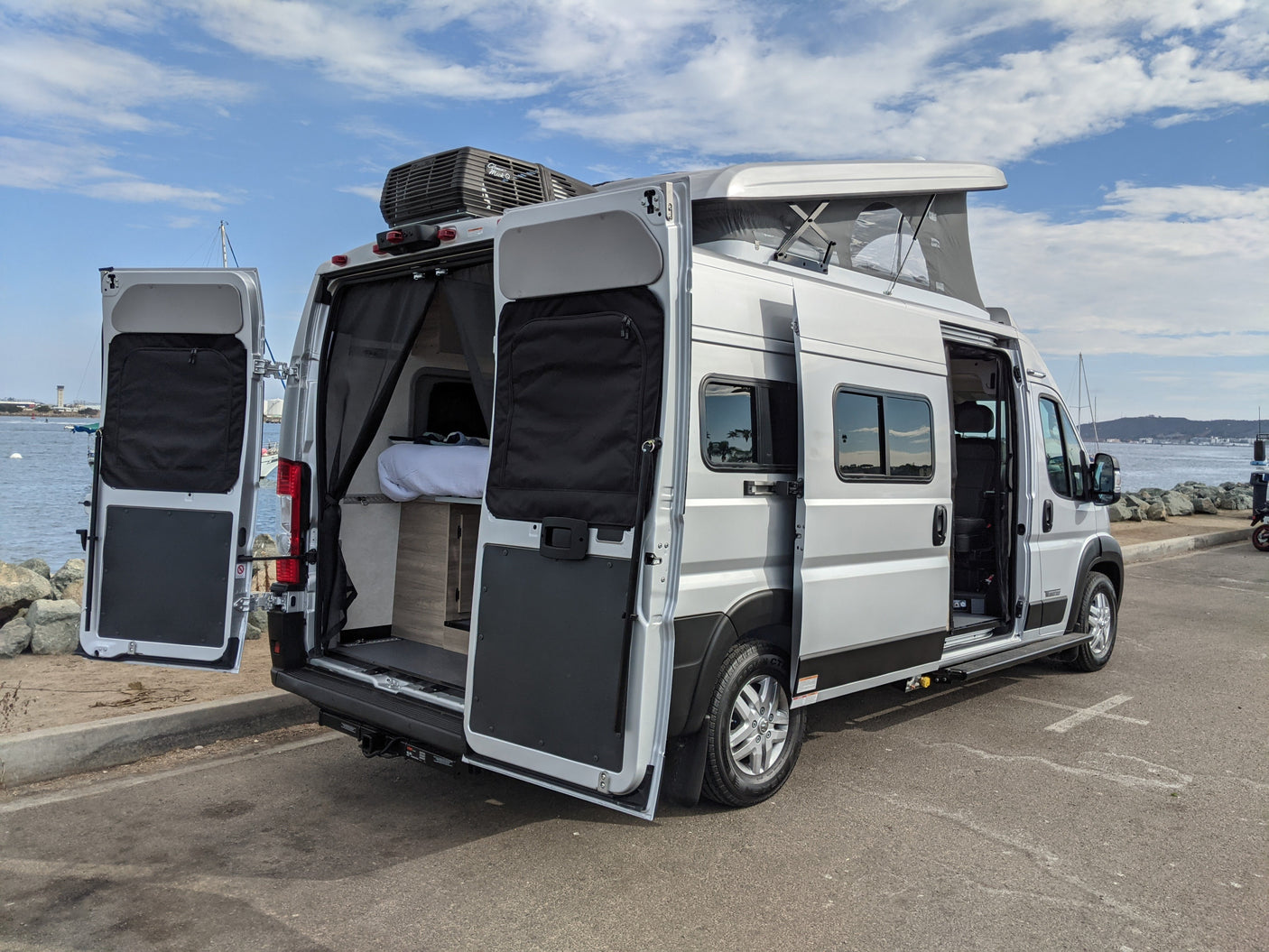 Silver rv rental camper van with open rear & side doors, revealing an interior bed & storage.