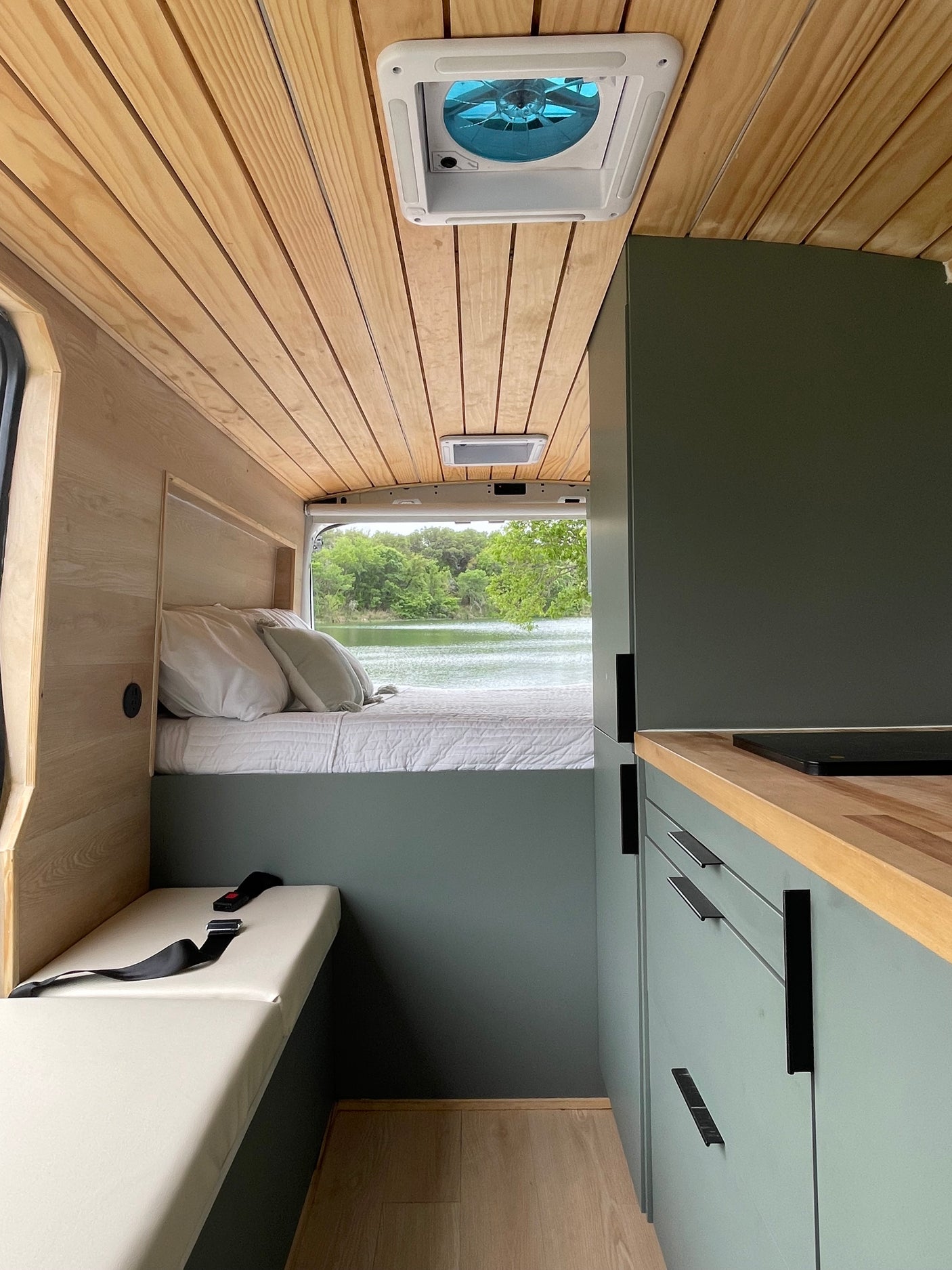 Cozy RV rental interior with custom wood walls, comfortable bed, compact kitchen, and a beautiful lake view from inside the van.