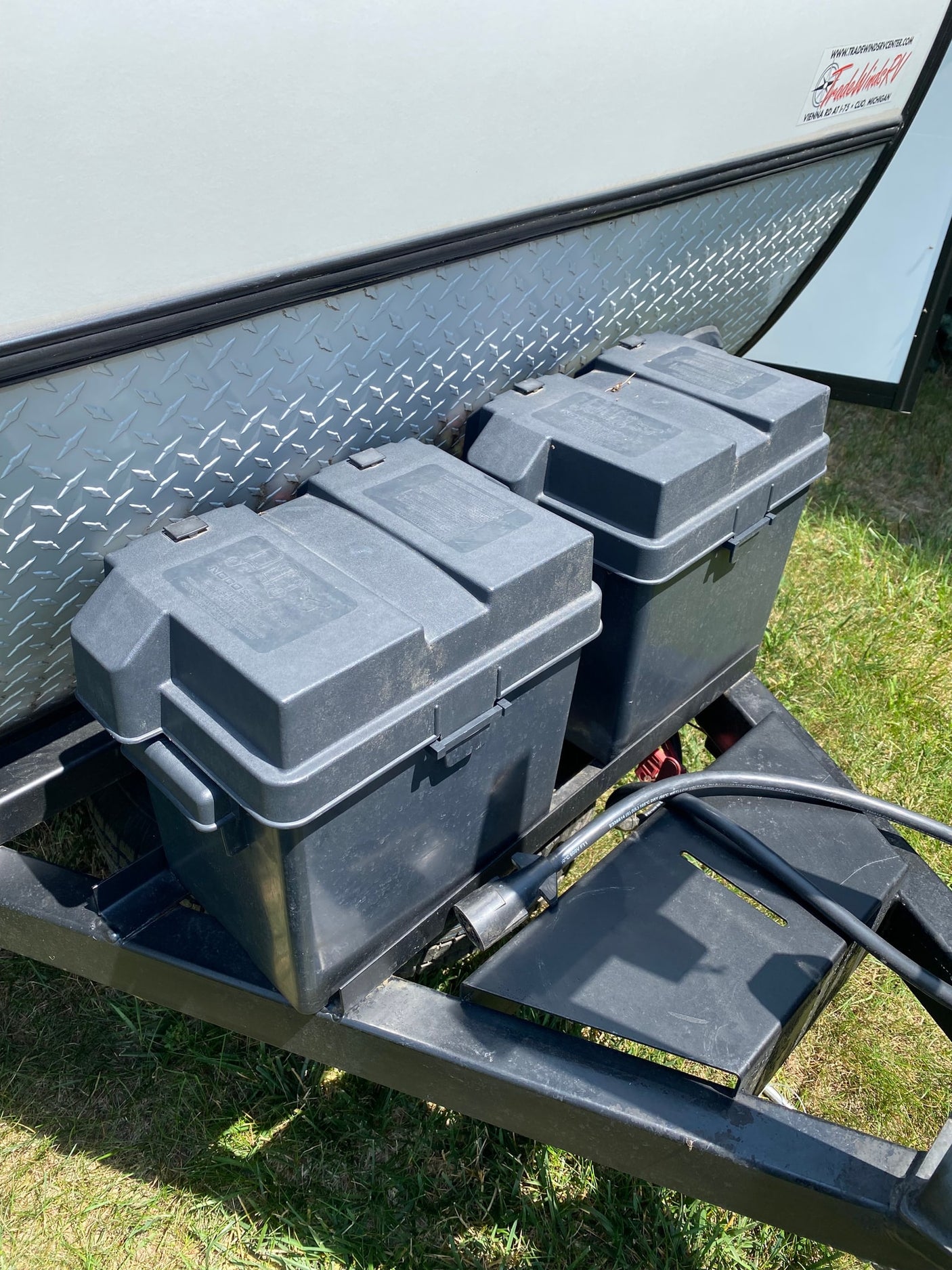 Front of an RV rental with two black battery boxes on the trailer hitch, featuring diamond plate siding and a sunny day.