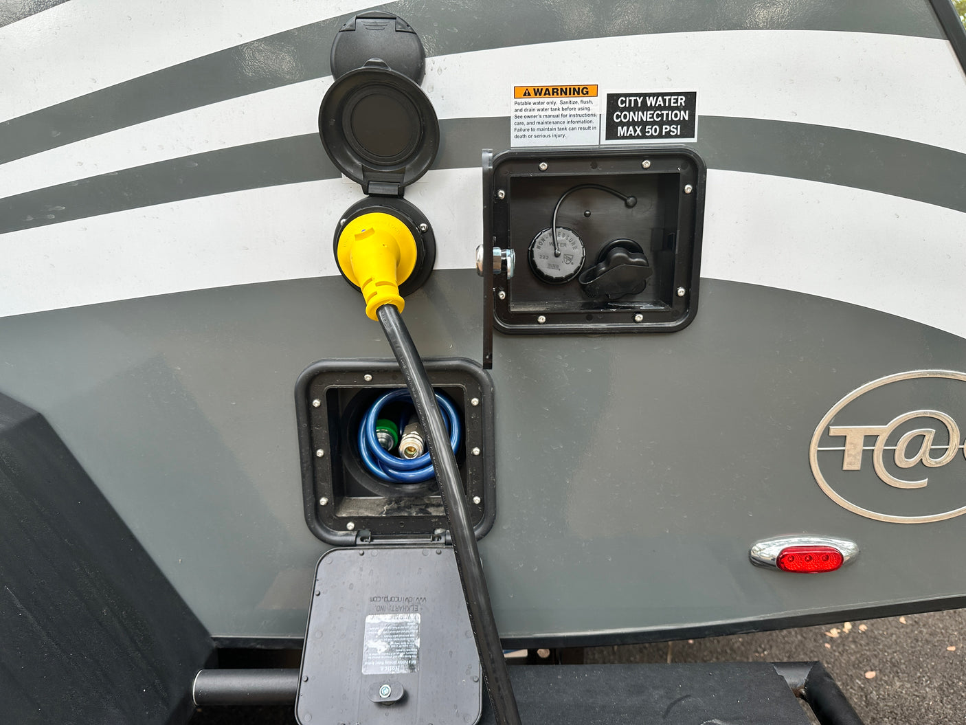 This RV rental's utility panel shows a yellow power cord, blue water hose, and city water connection with warning labels.