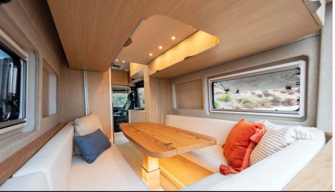 Comfortable RV rental interior featuring a bright dining area, wood table, and scenic window views for your road trip.