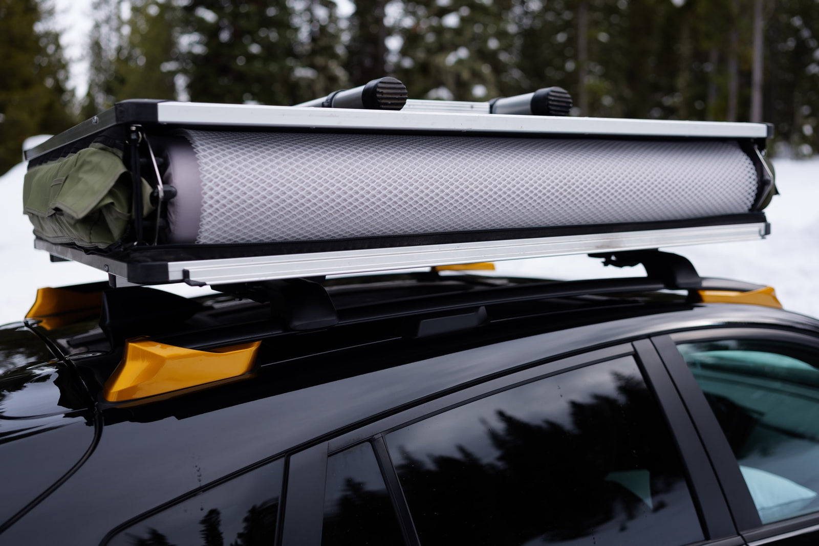 Packed rooftop tent on a black car's roof rack. A smart RV rental choice for agile snowy outdoor adventures.