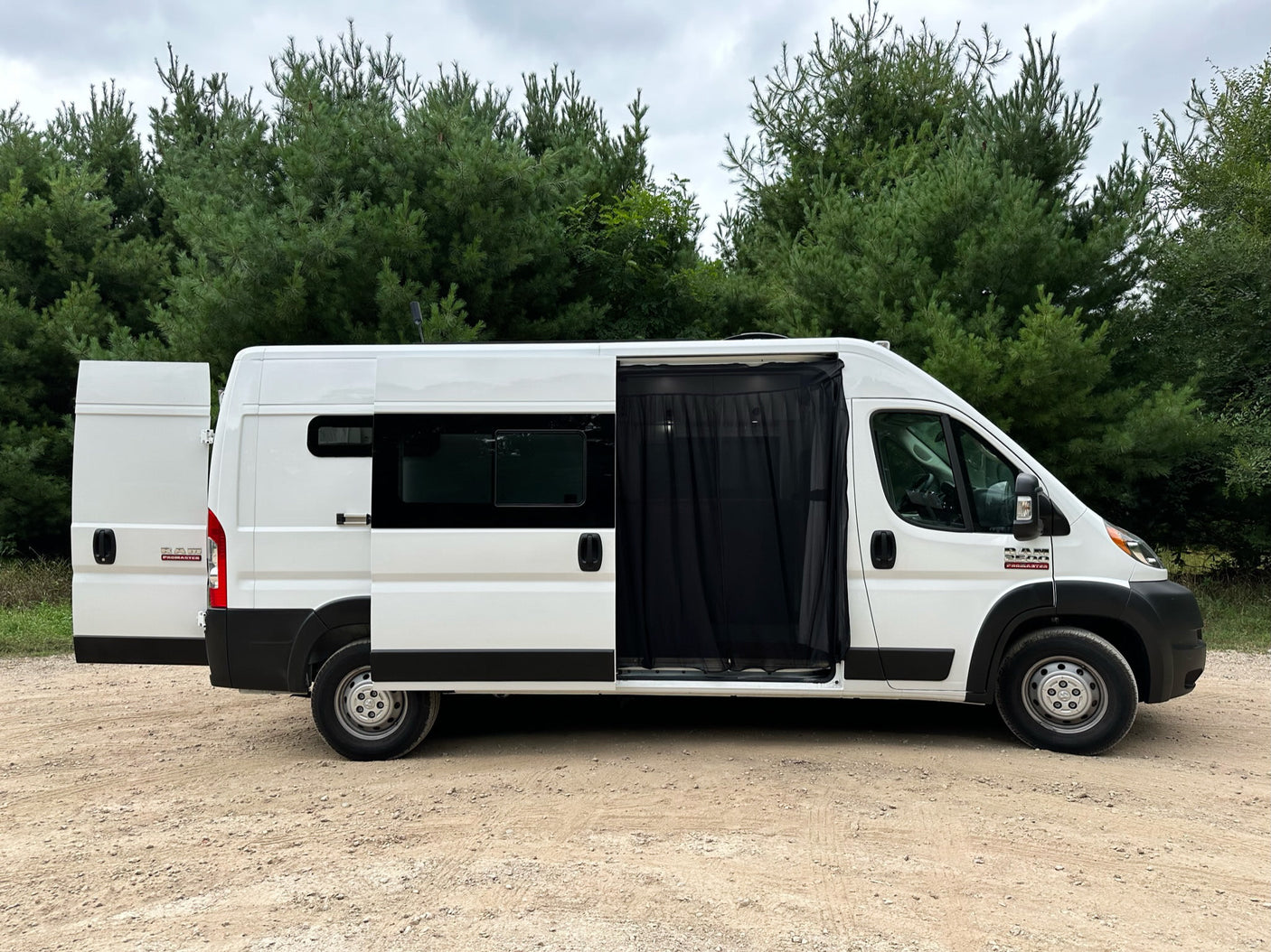 White camper van parked on dirt road, rear and side doors open with mesh screen. Ideal for RV rental trips.