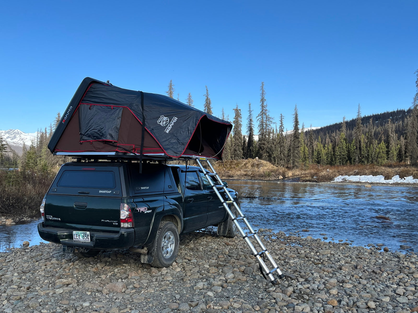 Green truck with iKamper rooftop tent by a river. Ideal rv rental for overlanding and enjoying remote camping in nature.