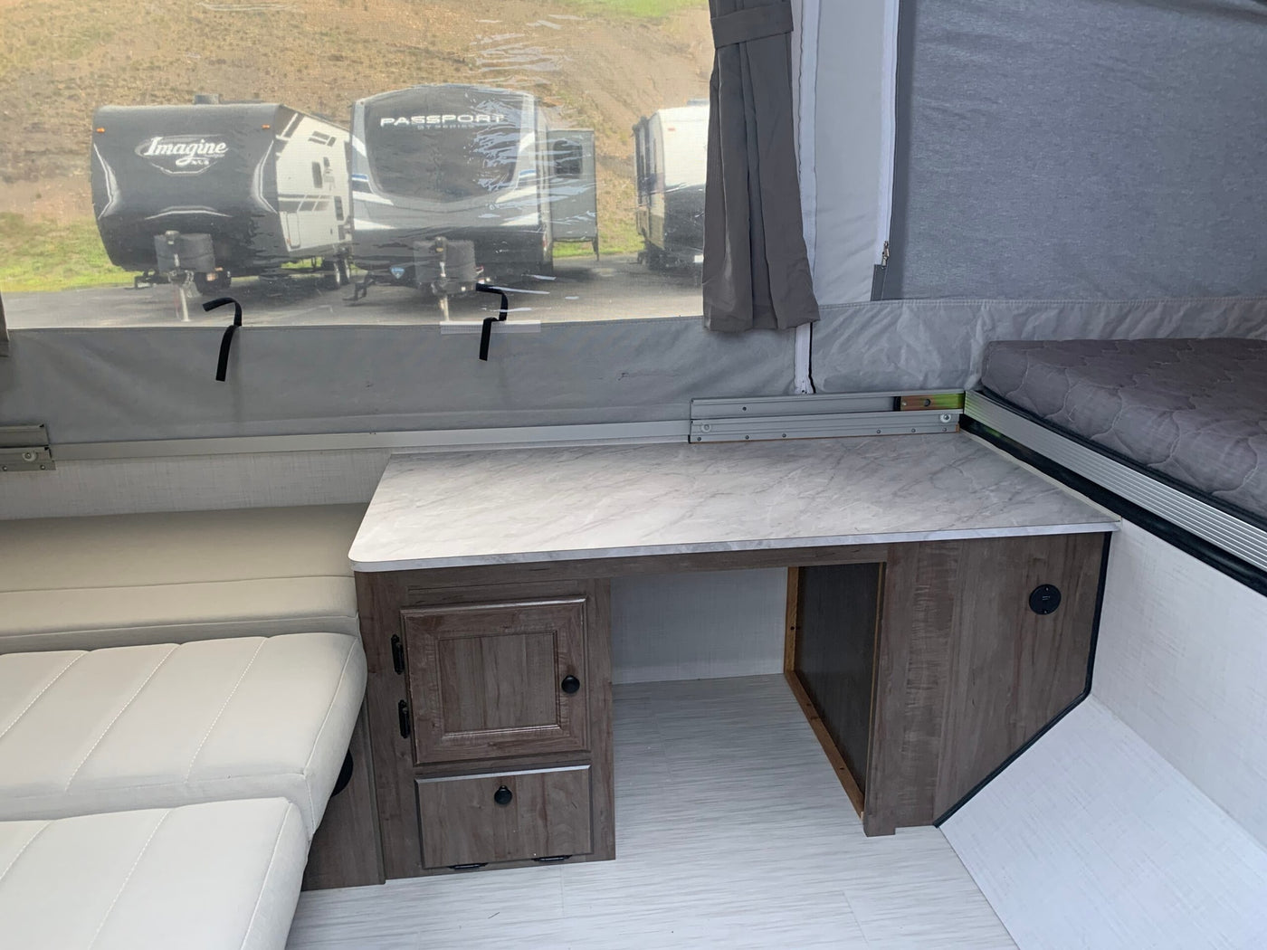 Inside this RV rental: a pop-up camper with a desk, storage, comfy seating, and a bed, overlooking other travel trailers. — photo 6