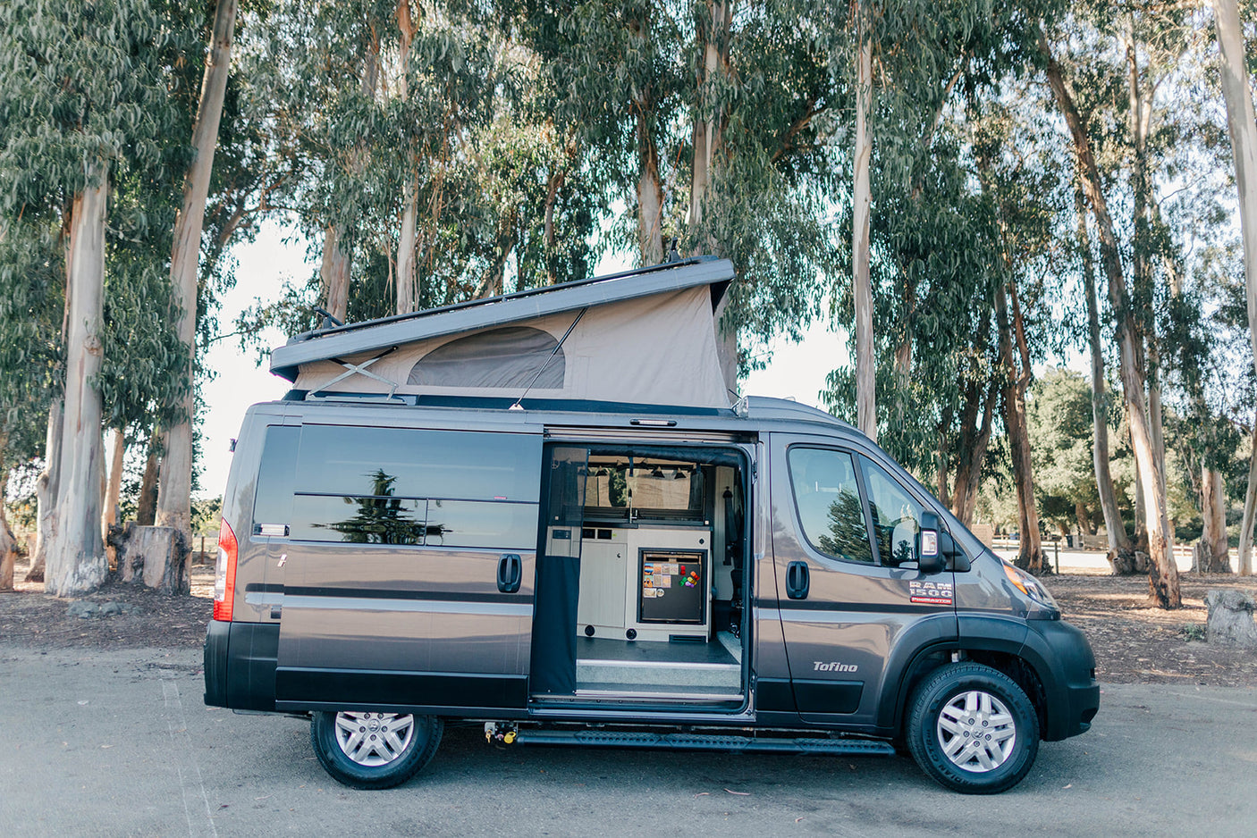 Gray Ram ProMaster camper van rv rental with pop-top up, side door open, revealing compact kitchen. Ideal for adventure.