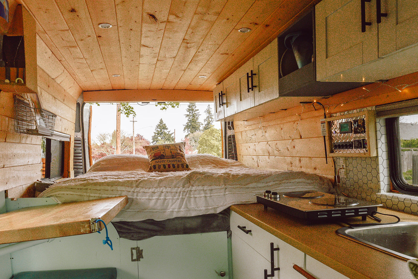 Inside a cozy wood-paneled campervan featuring a bed, kitchen with a hot plate, and control panel. Ideal for an RV rental.