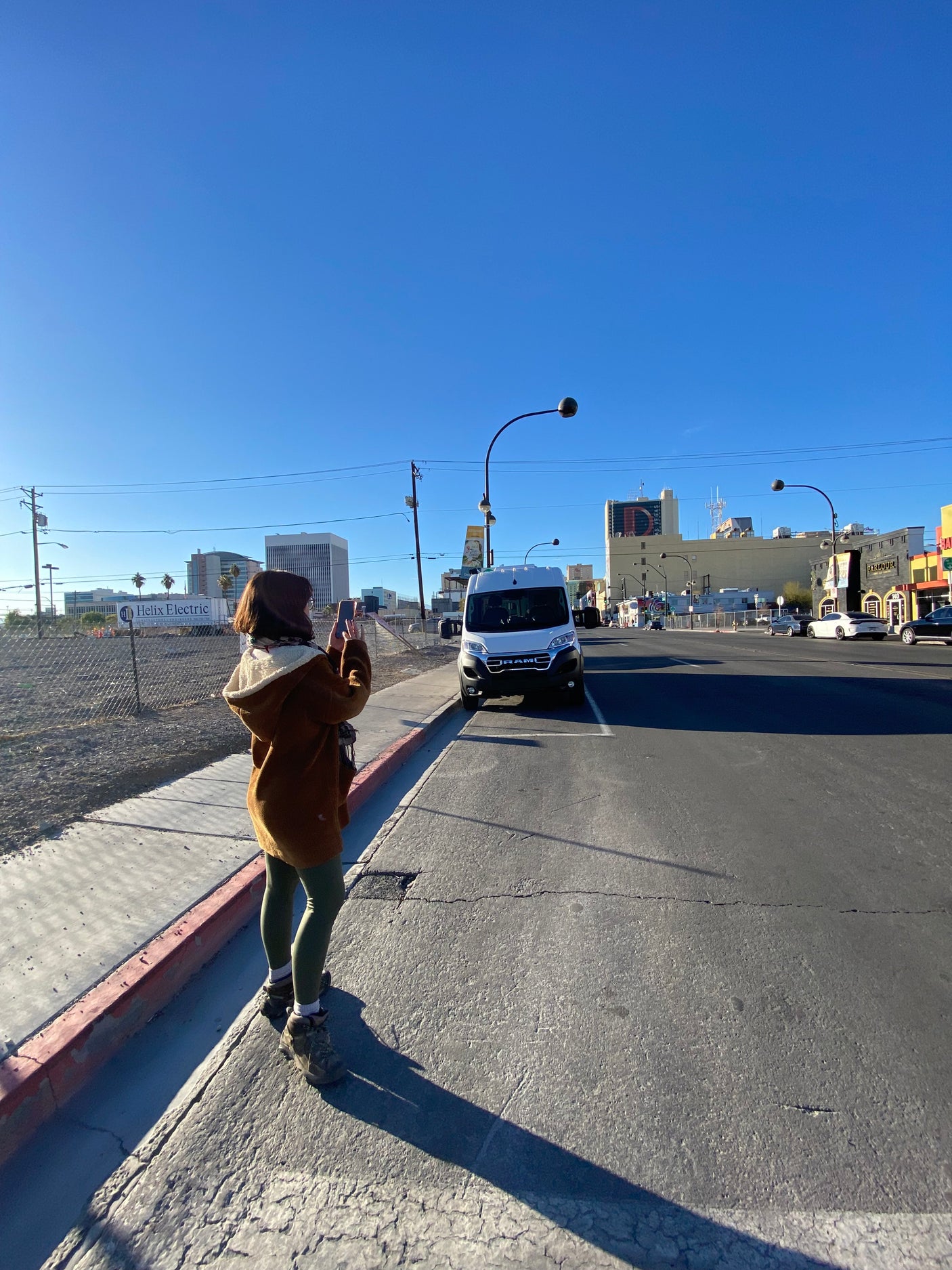 A white Ram van, an RV rental option, parked on a sunny Las Vegas street. A person captures the city view.