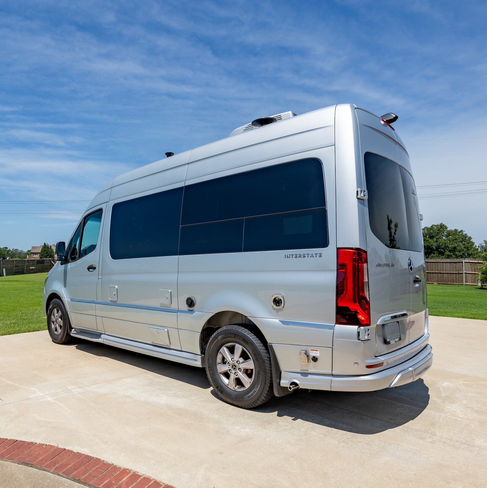 parked on a sunny concrete driveway beside a house.|A silver Airstream Mercedes-Benz Sprinter RV rental van parked on a concrete driveway in bright sunlight.|This silver Mercedes-Benz Sprinter RV rental van is parked on a sunny paved driveway.|Silver Airstream Interstate RV