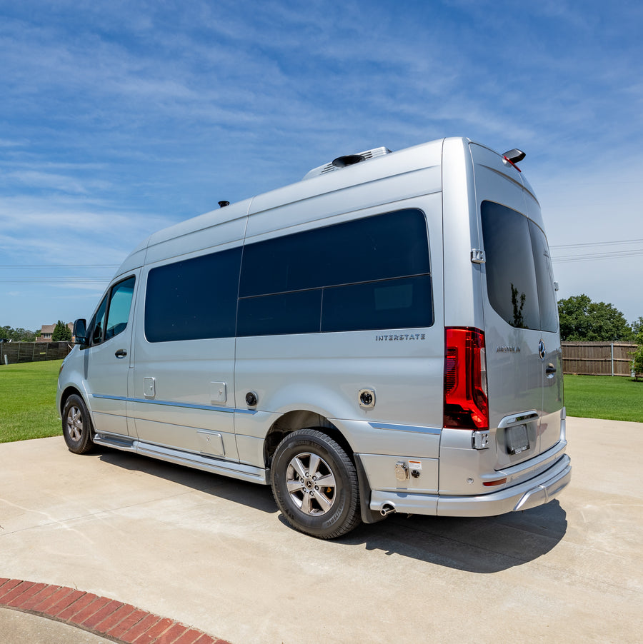 parked on a sunny concrete driveway beside a house.|A silver Airstream Mercedes-Benz Sprinter RV rental van parked on a concrete driveway in bright sunlight.|This silver Mercedes-Benz Sprinter RV rental van is parked on a sunny paved driveway.|Silver Airstream Interstate RV