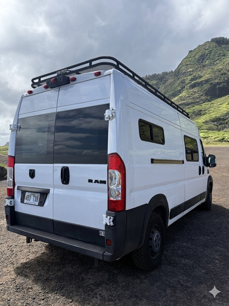 This white RAM camper van with a roof rack, ideal for your next rv rental adventure by lush green mountains under cloudy skies.