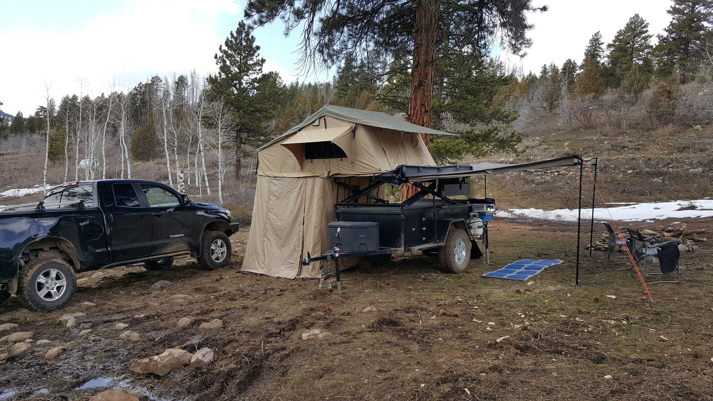 RV rental for rugged overlanding: A truck & trailer with rooftop tent and annex set up in a muddy, snowy forest campsite.