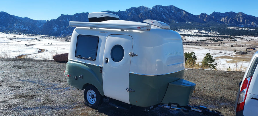 RV rental: A cozy Happier Camper travel trailer parked overlooking a beautiful snowy mountain landscape, perfect for adventure.