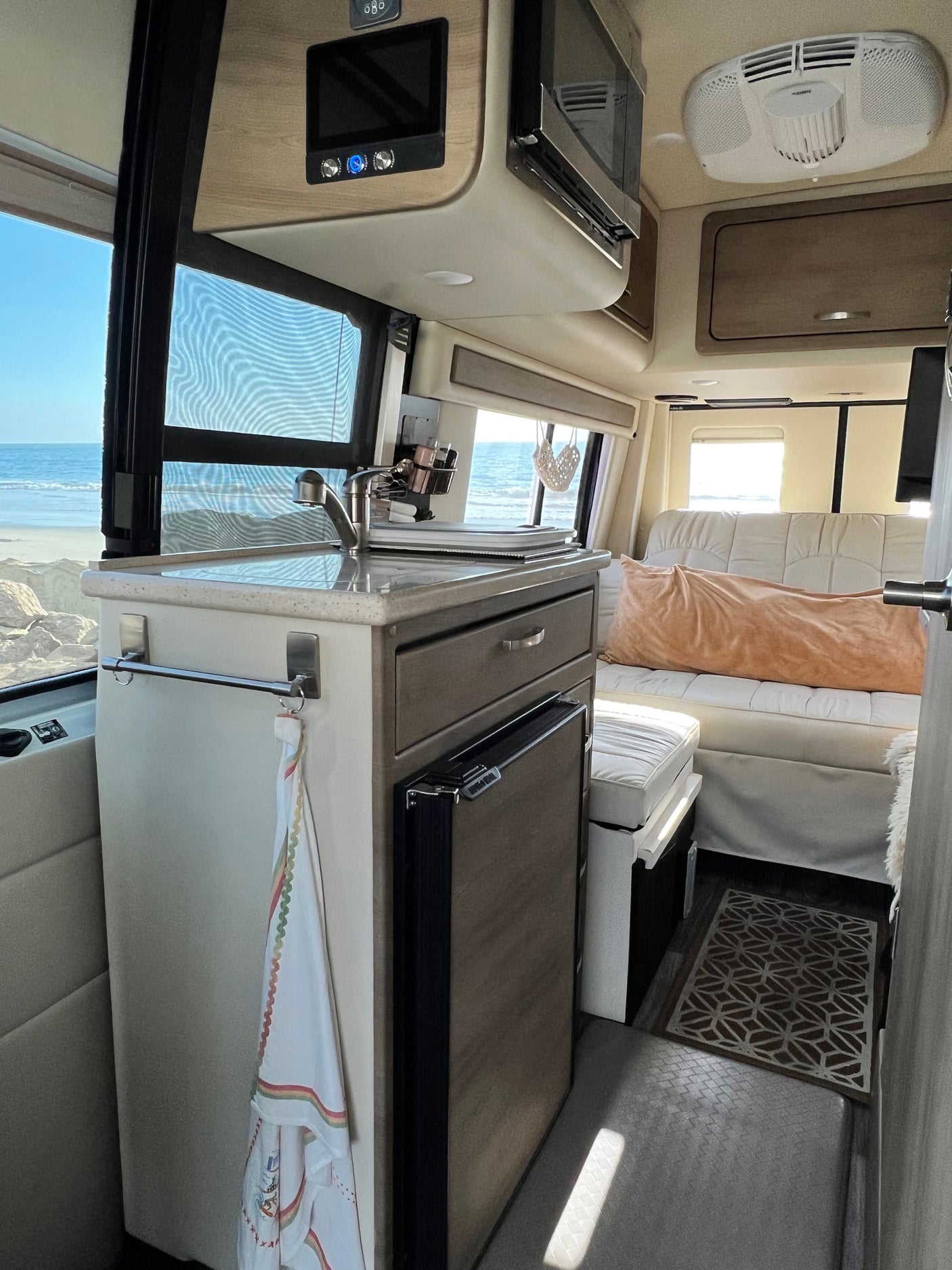 Inside a luxurious RV rental: full kitchen with fridge, modern controls, and a breathtaking ocean view. Perfect for travel.