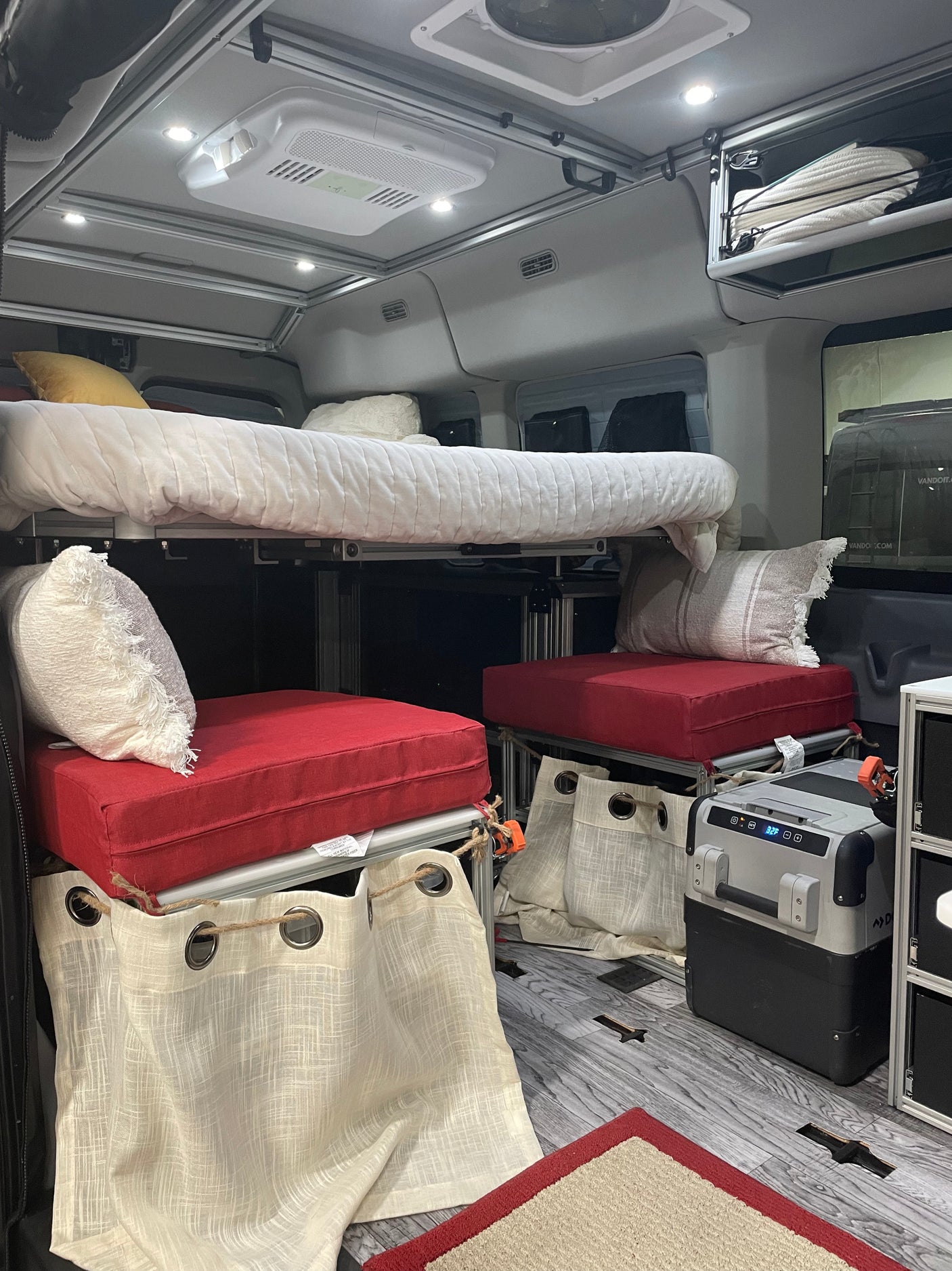 RV rental interior showcasing a bunk bed system, lower seating with red cushions, fridge, and overhead lighting.