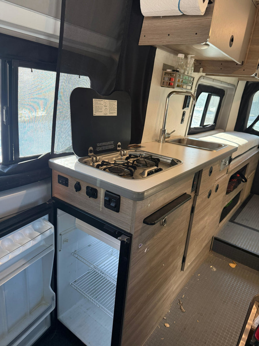 RV rental kitchen: compact 2-burner stove, sink, and open fridge. Ready for your mobile cooking adventures!