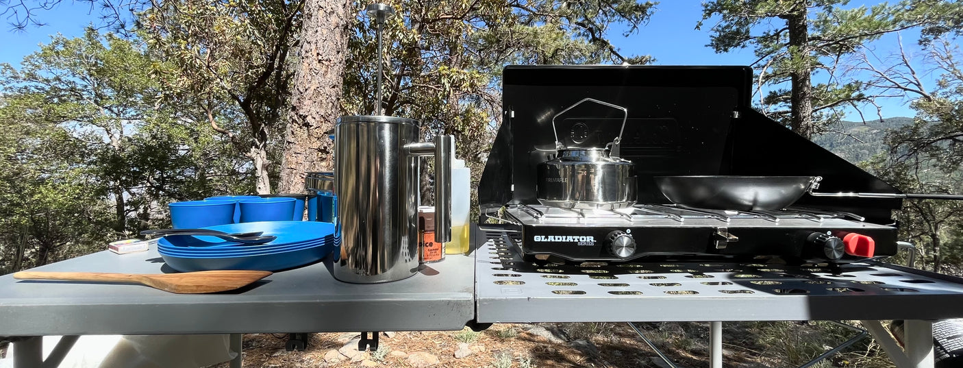 Enjoy camping meals with our RV rental! Outdoor kitchen includes a portable stove, kettle, French press, and blue dishes.