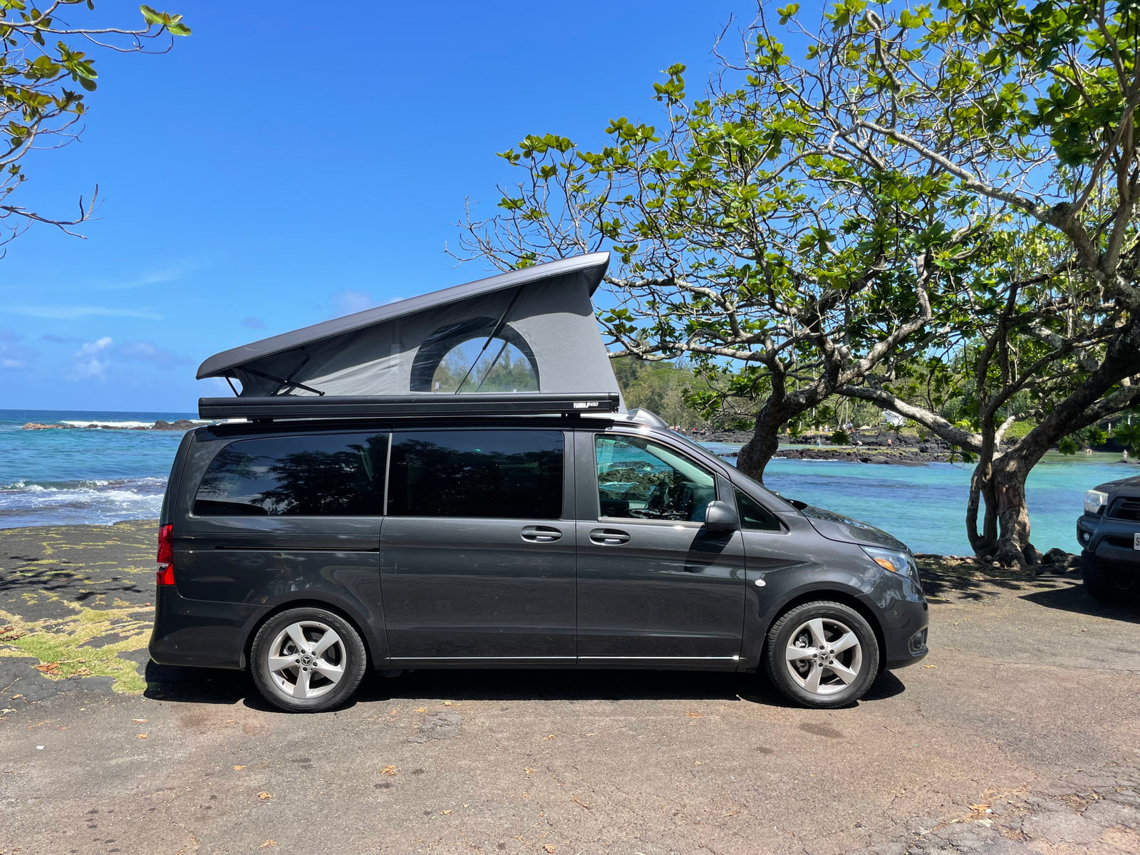Explore scenic coasts! This dark grey camper van, an ideal rv rental with pop-top extended, enjoys a beautiful ocean view.