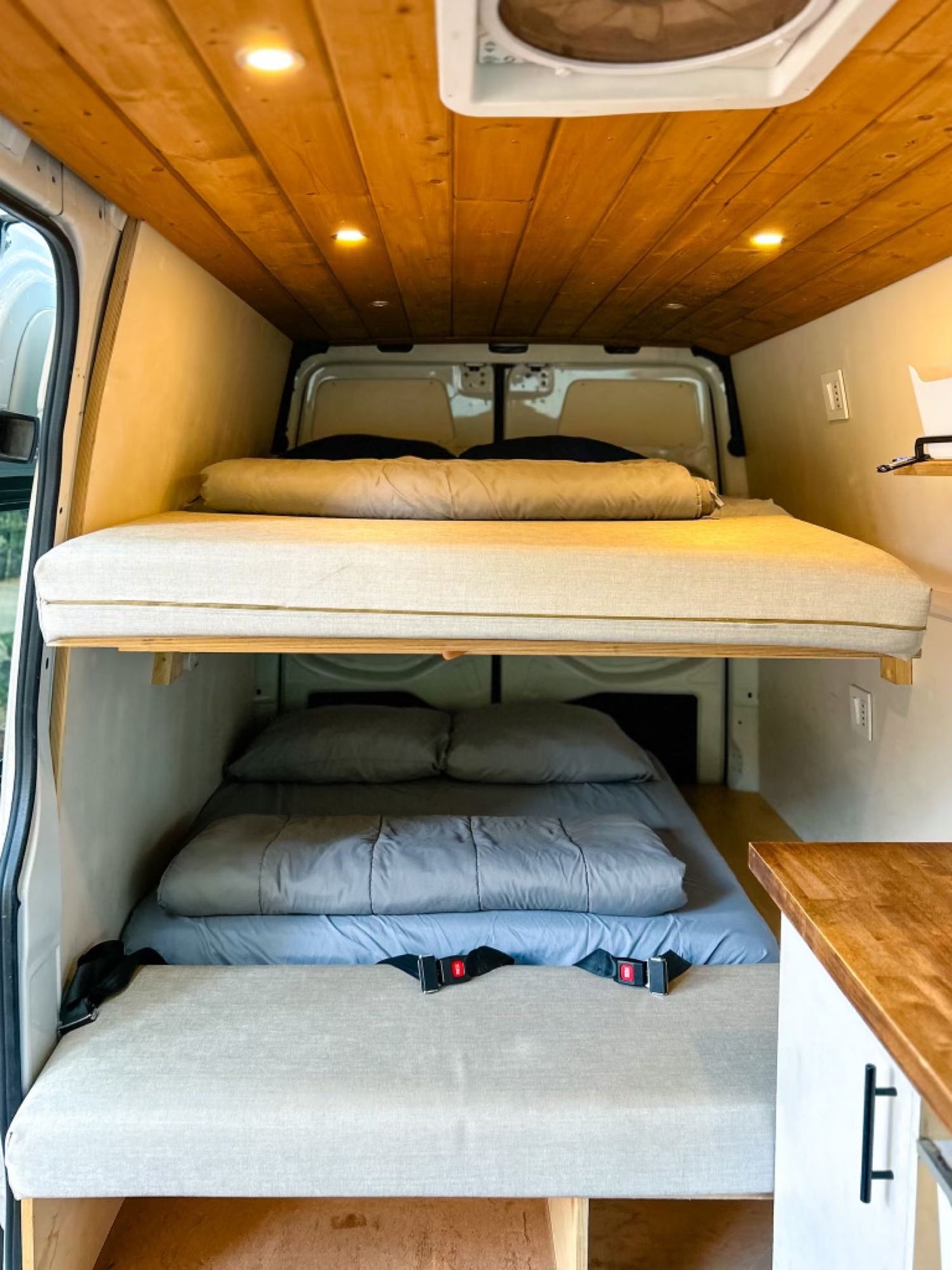 RV rental interior featuring tiered bunk beds with clean bedding, a wood plank ceiling, & recessed lighting. Perfect for travel.