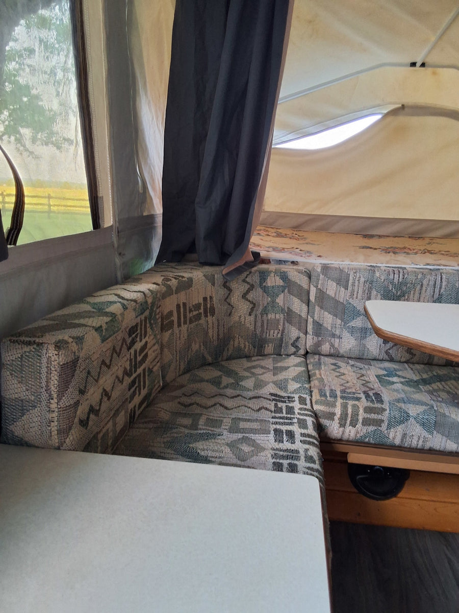 Cozy RV rental interior with patterned dinette, bright window view, and open bunk space.