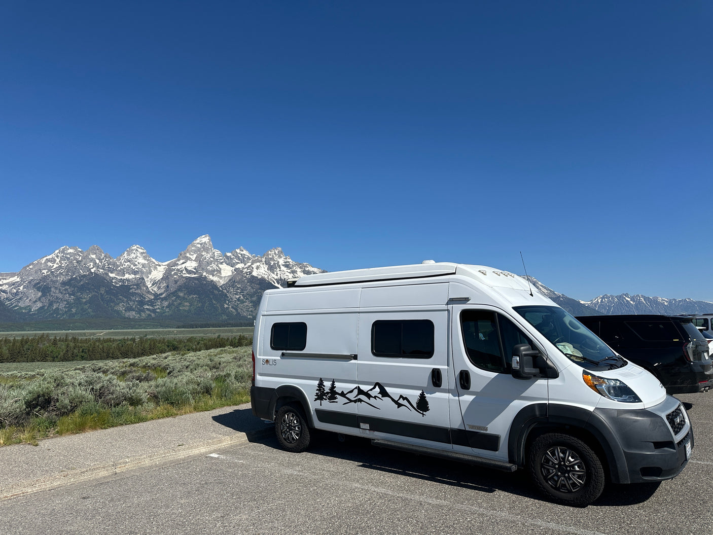 Scenic RV rental adventure! White camper van parked with stunning snow-capped mountains in the background under a clear blue sky.