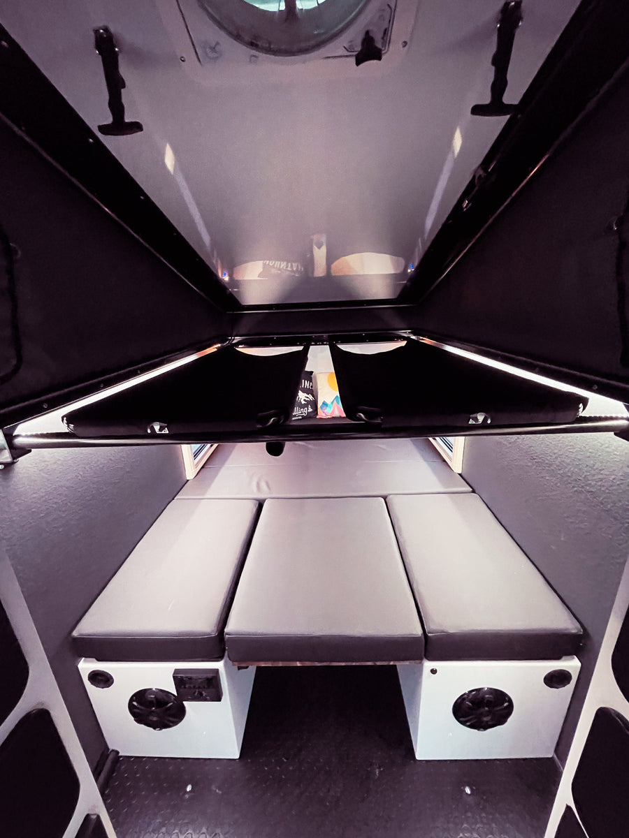 Explore the compact RV rental interior, featuring a versatile sleeping area with three gray cushions and built-in amenities.