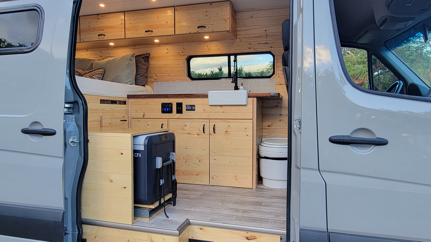 Step into this custom RV rental: light wood interior, kitchen, bed, pull-out fridge & toilet. Ideal camper van setup.