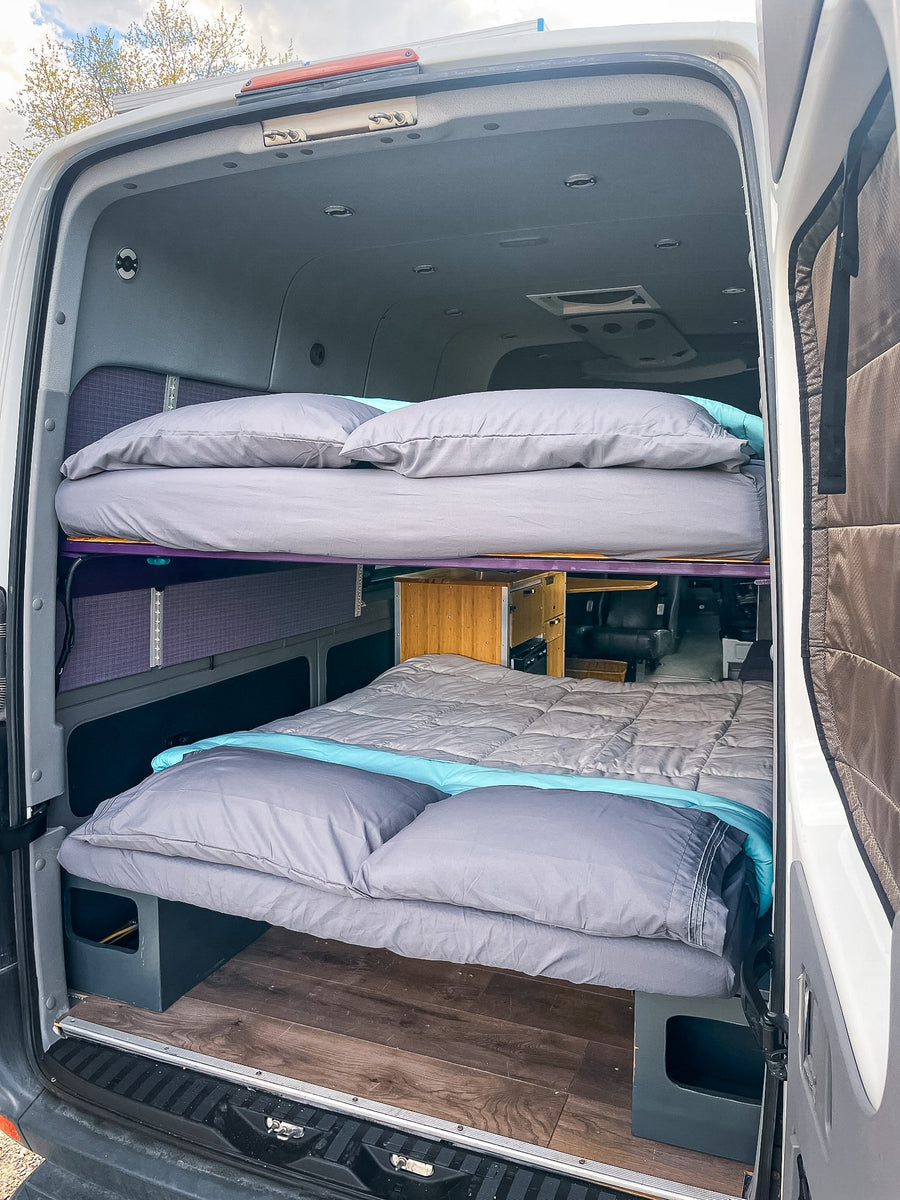 RV rental's cozy interior: a bunk bed with grey & blue bedding offers comfy rest for your next adventure.