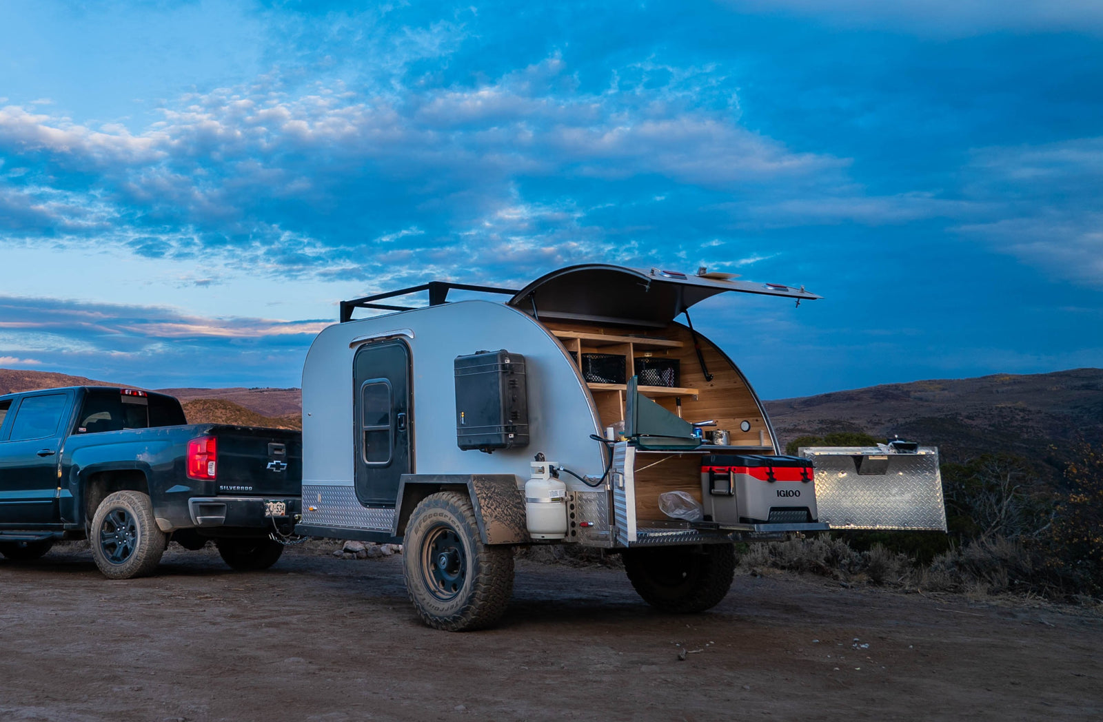 Adventure-ready RV rental: A pickup truck tows a teardrop trailer with an open outdoor kitchen, perfect for remote camping.