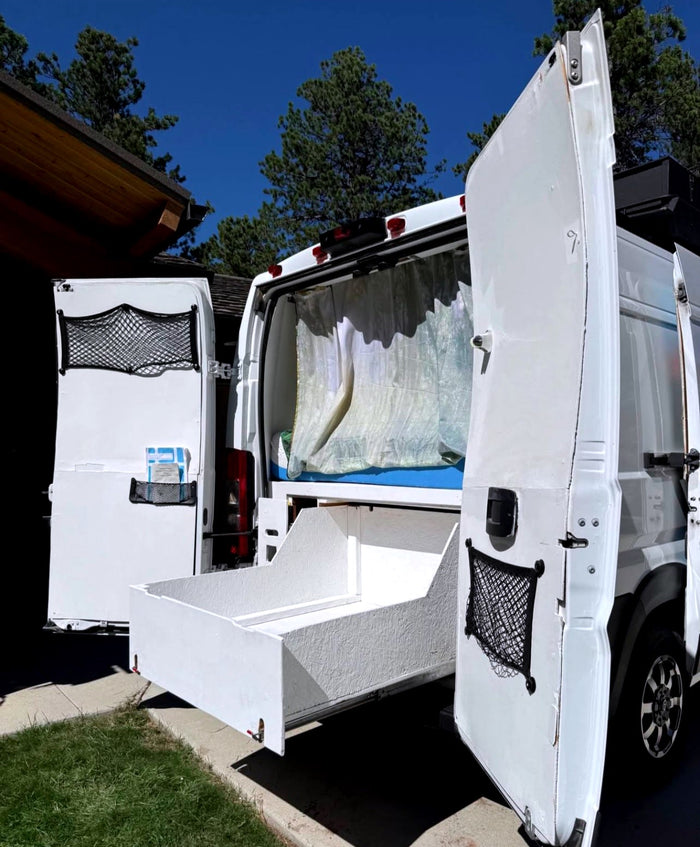 parked by pine trees.|White Ram ProMaster RV rental van