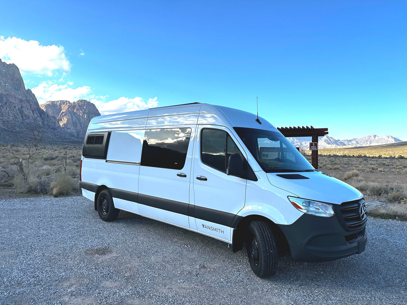 This white VANSMIth RV rental van is parked in a vast desert with rugged mountains, ready for adventure.