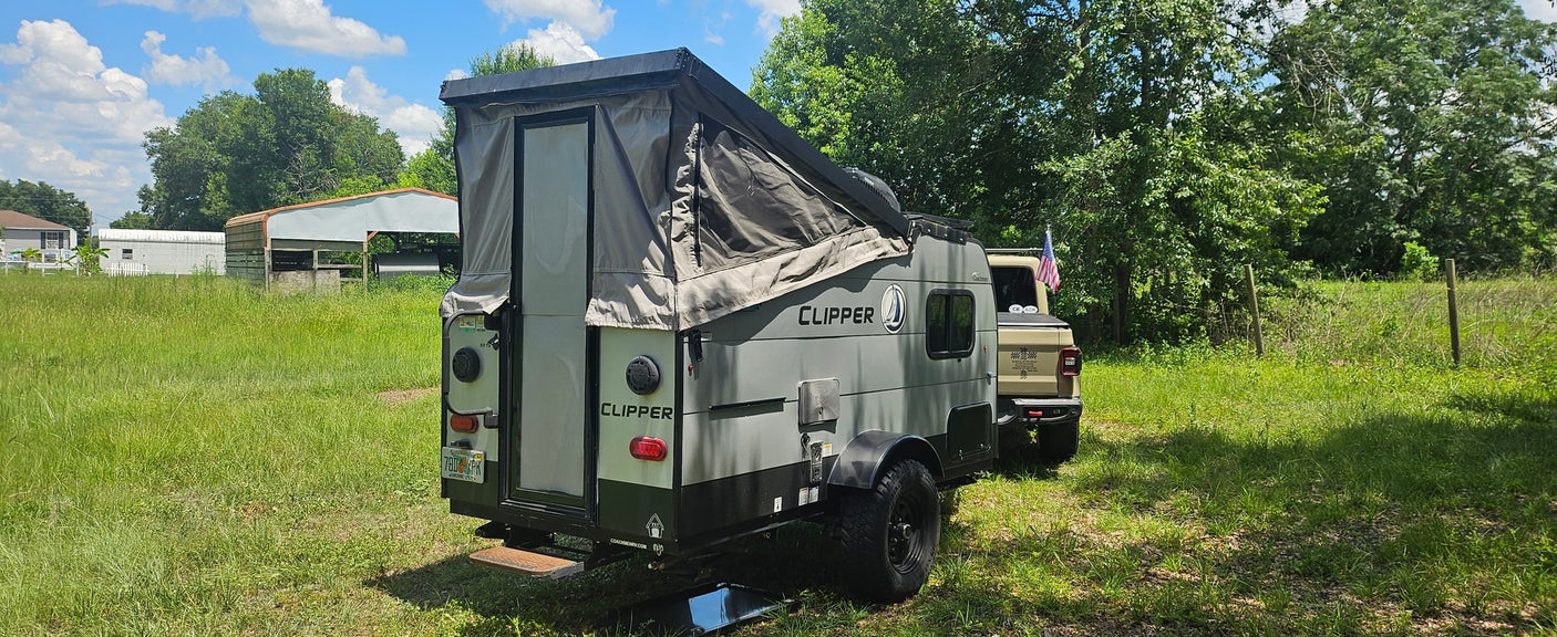 Clipper pop-up camper, ideal for your next RV rental, parked in a sunny, grassy field hitched to a tan truck.