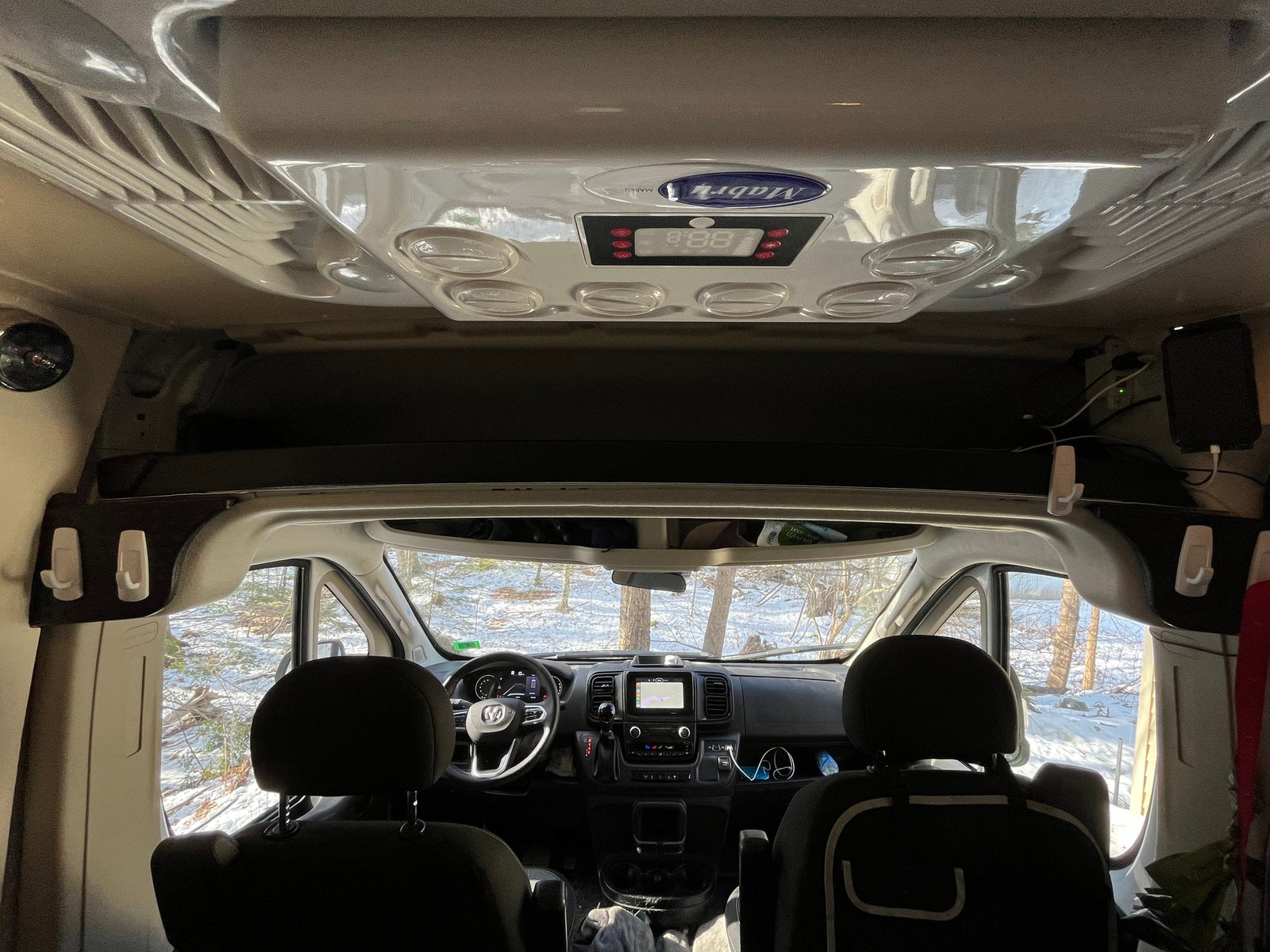 RV rental interior: looking forward in a camper van, showing the dashboard and a snowy forest outside.