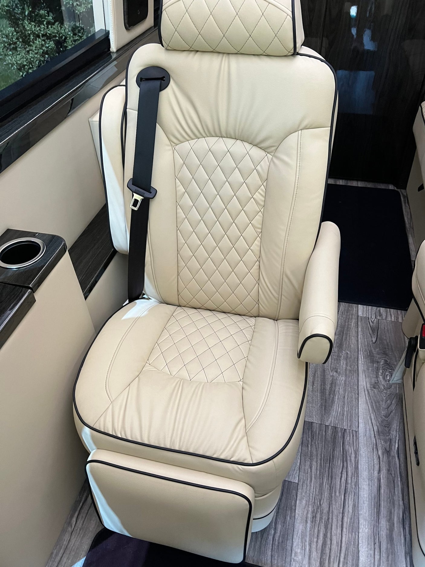 Luxury RV rental: Enjoy the comfort of a cream-colored, quilted leather seat with a cup holder and wood flooring.