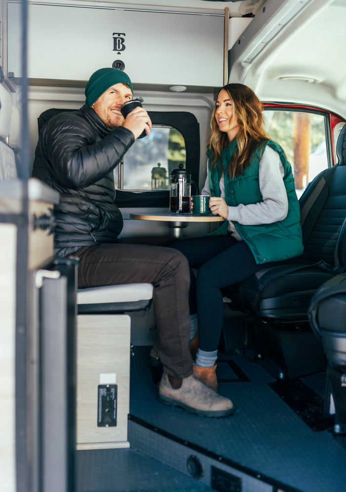 A joyful couple enjoys coffee inside their modern RV rental, perfect for cozy road trips and camping adventures.