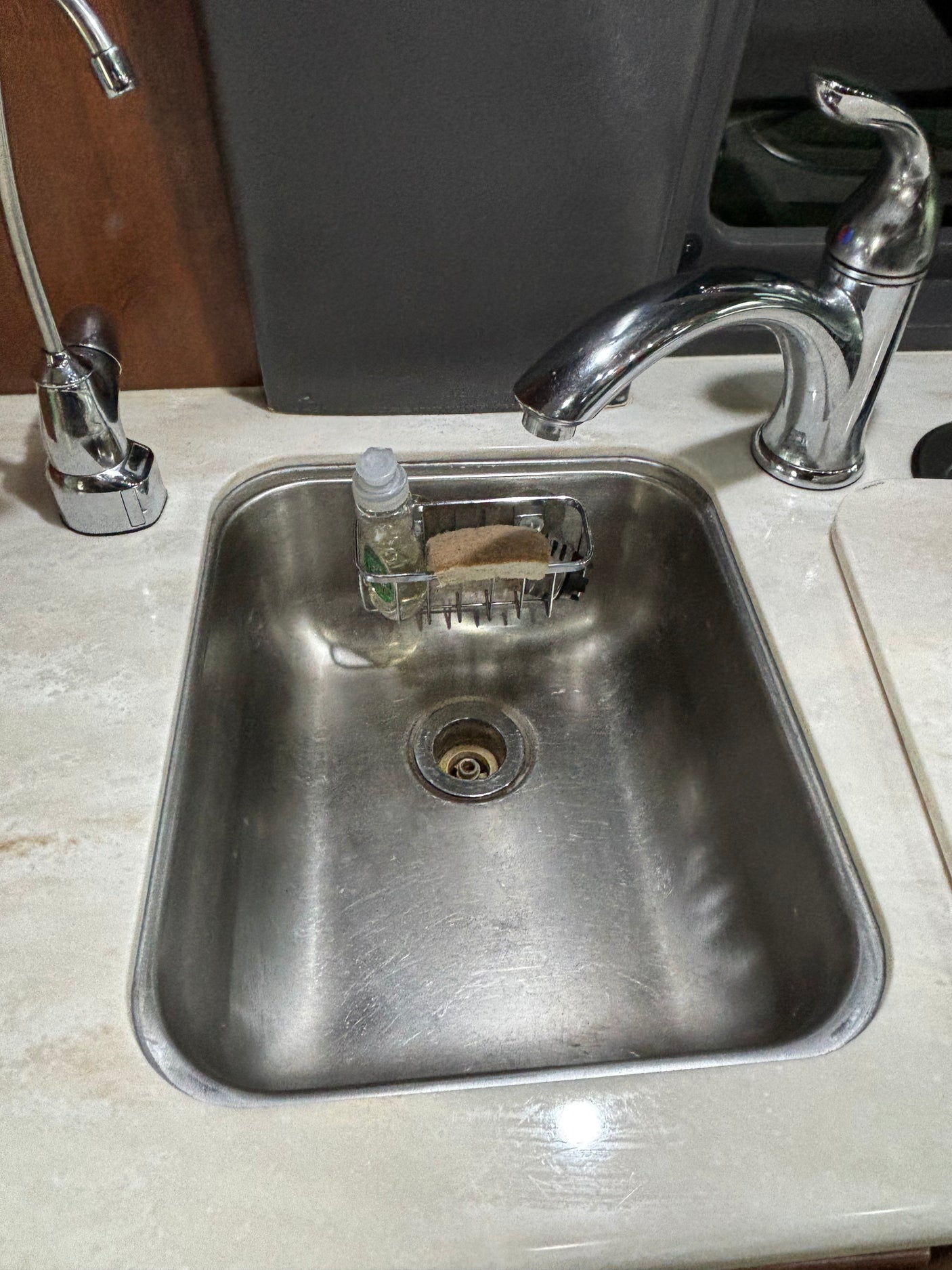 Compact stainless steel sink, faucets, soap dispenser, and sponge in an RV rental kitchen area.