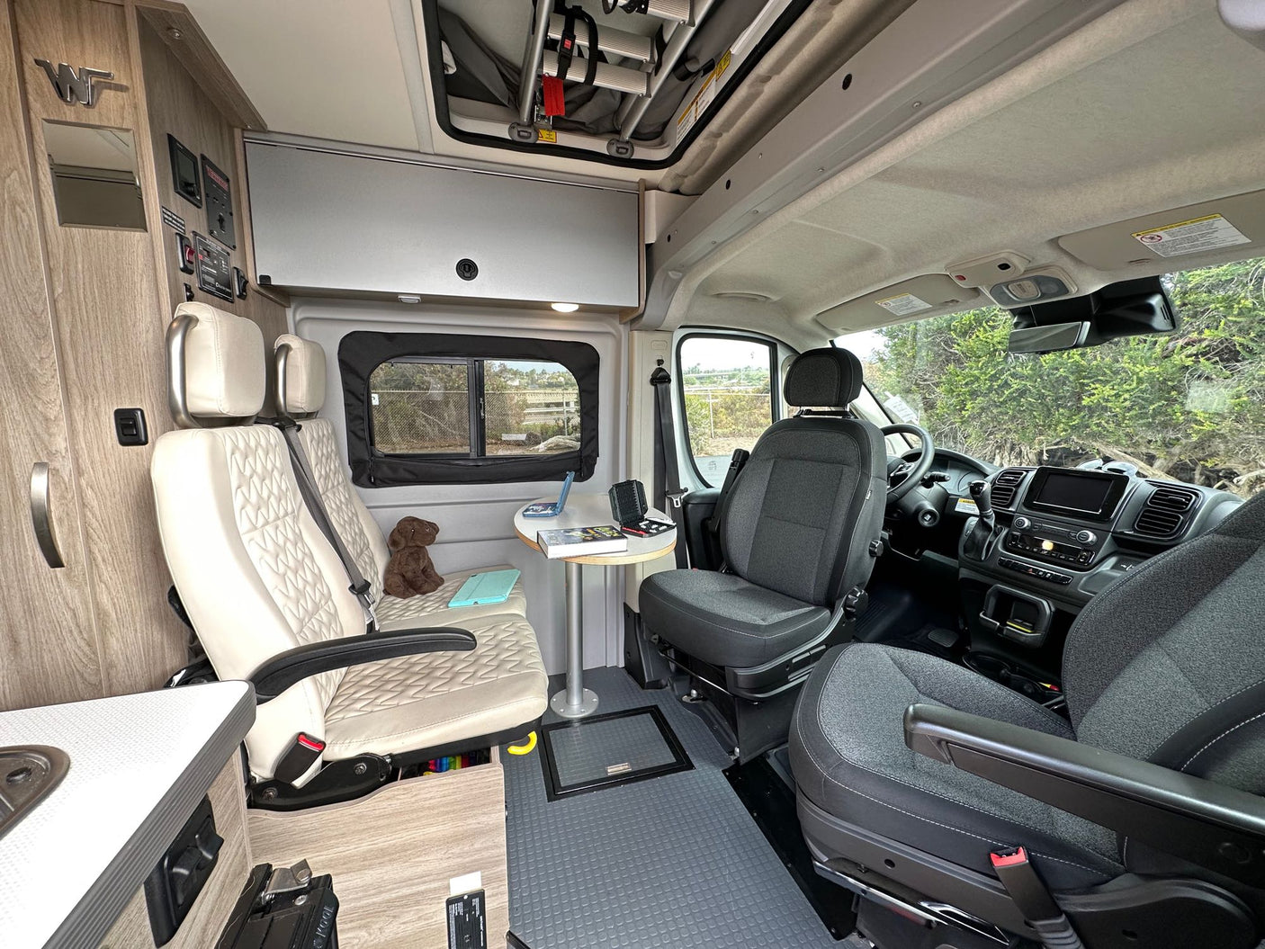 Inside this RV rental, see swivel front seats, comfy living area, table, and overhead storage for mobile living.