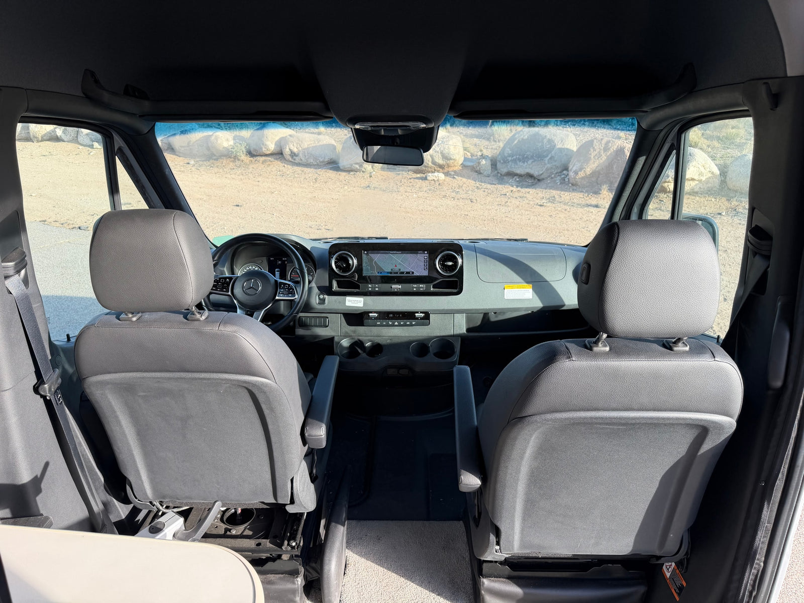 Front cabin view of an rv rental, featuring driver & passenger seats, dashboard with navigation, and a windshield with visible cracks.
