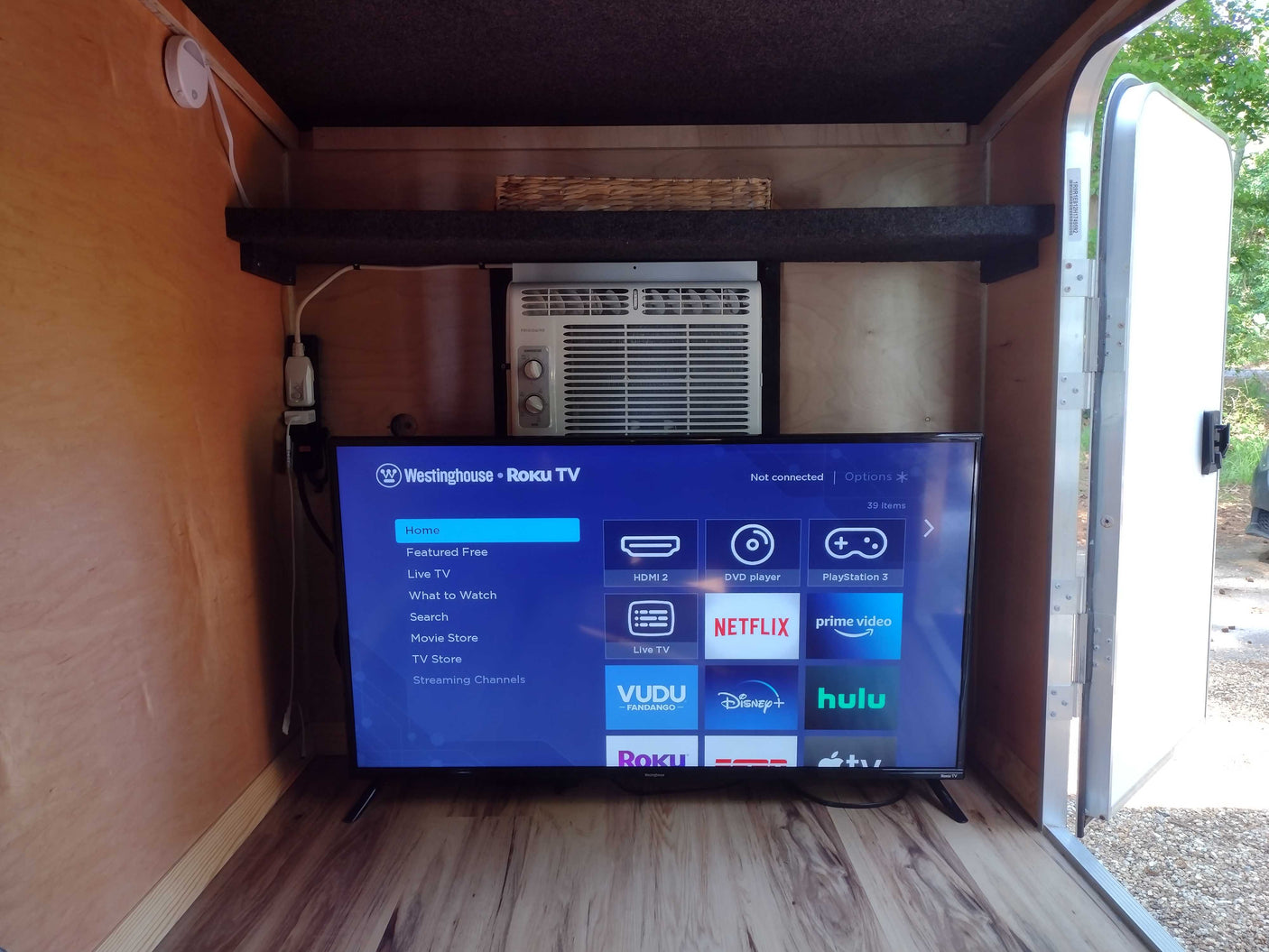 Compact RV rental interior featuring a Roku TV, AC, and shelf. Ideal for cozy entertainment in a travel trailer setup.