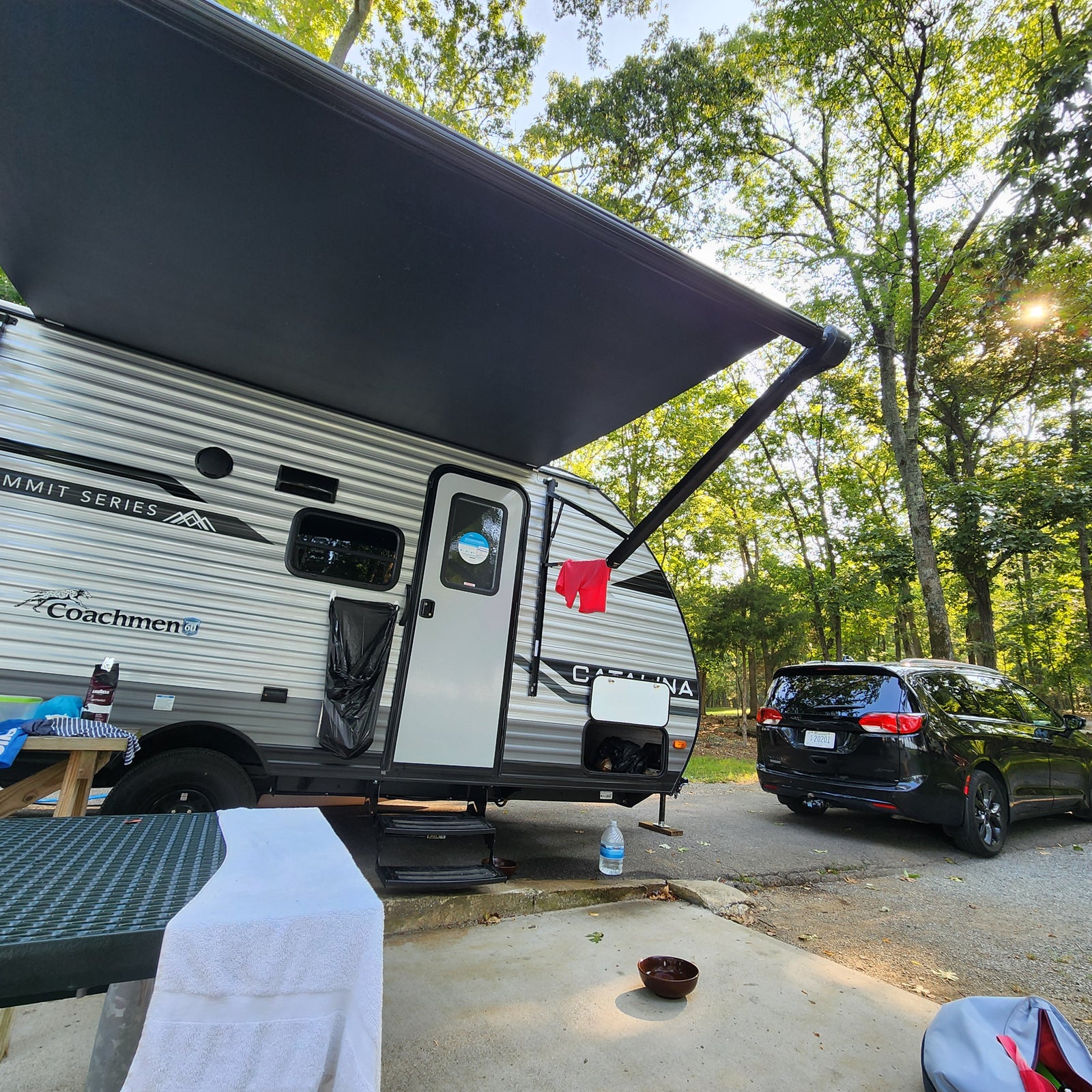 Sunny campsite scene with an RV rental, featuring a travel trailer, car, and picnic table.