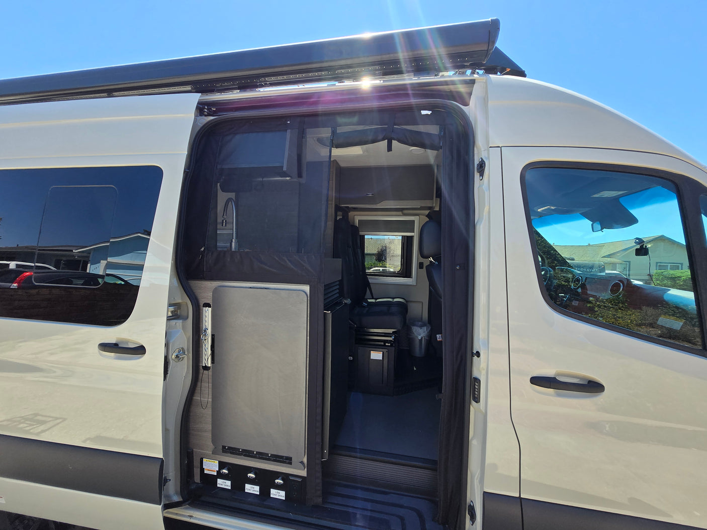 This RV rental's open side door reveals a compact interior with a sink, fridge, and seating, ready for mobile adventures.