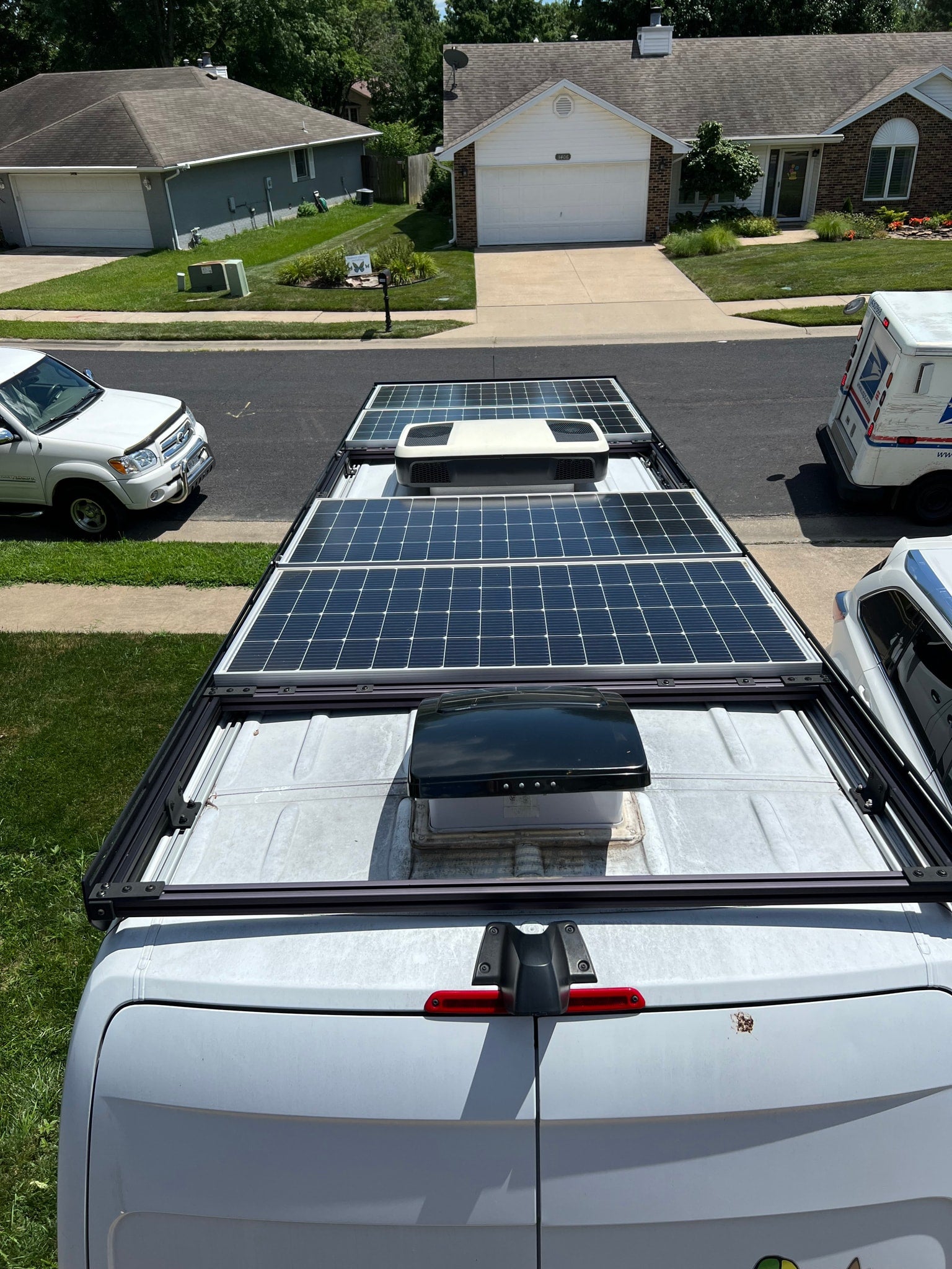 Overhead view of an RV rental van with solar panels & AC unit on its roof, parked on a residential street.