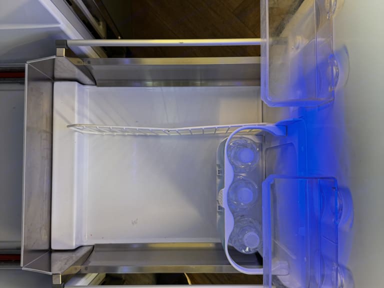 Inside an RV rental fridge: clear shelves, water bottles, and a blue interior light for your travel convenience.