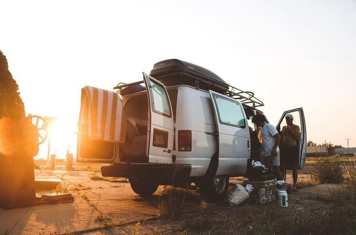 facing an epic mountain view and waterfall from open van doors. Ideal for adventure travel.|Two men organize gear in a white **RV rental** van at sunset