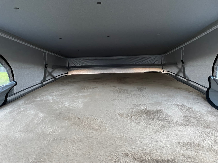 An RV rental's cozy pop-top sleeping area. A plush, light-colored bed fills the frame, surrounded by fabric tent walls.