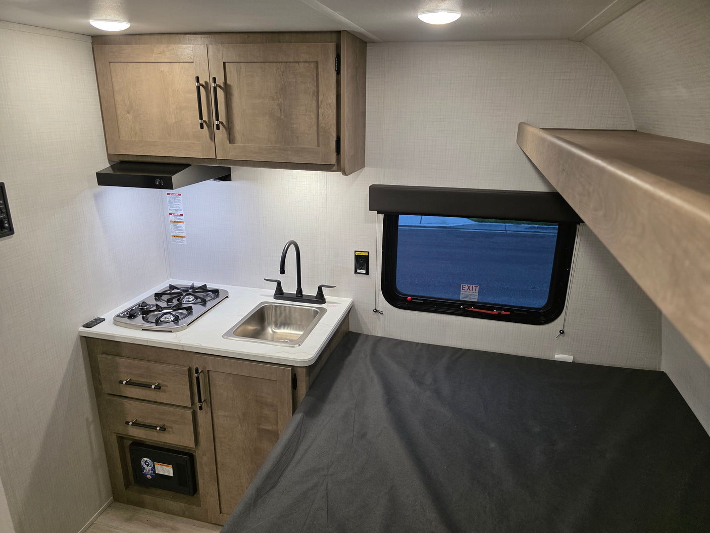Compact RV rental interior featuring a kitchen with stove/sink, bunk bed, and lower sleeping area, ideal for travel.