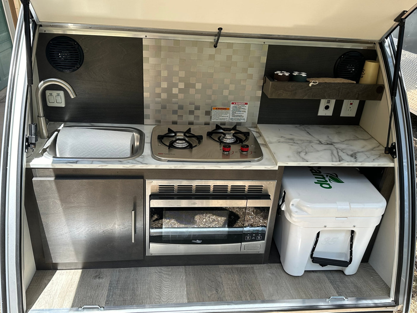 and a chair invite relaxation.|A compact RV rental teardrop trailer parked in a serene forest setting