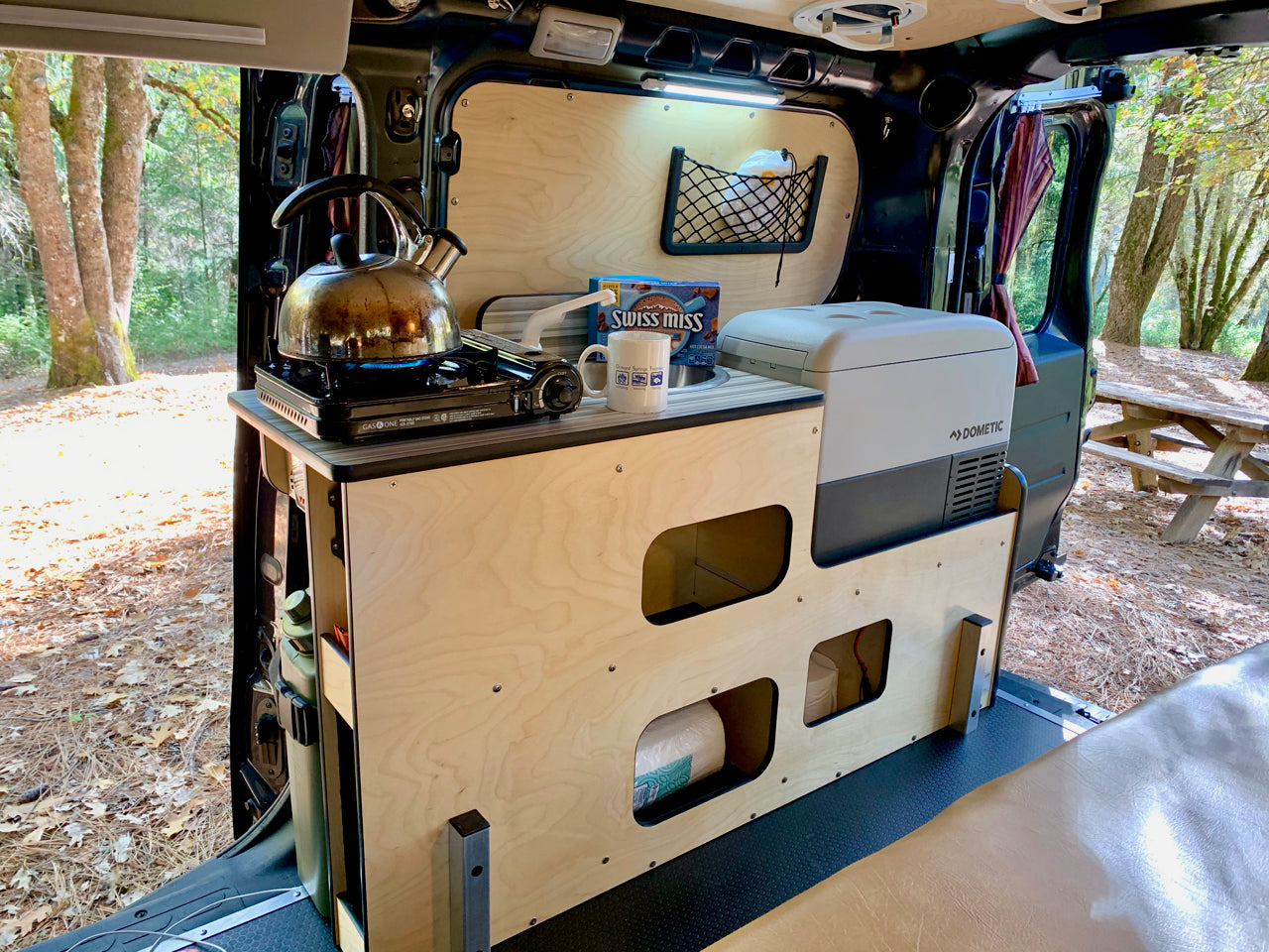 This rv rental features a well-equipped mobile kitchen with a camping stove, kettle, Dometic fridge, and organized storage for adventures.