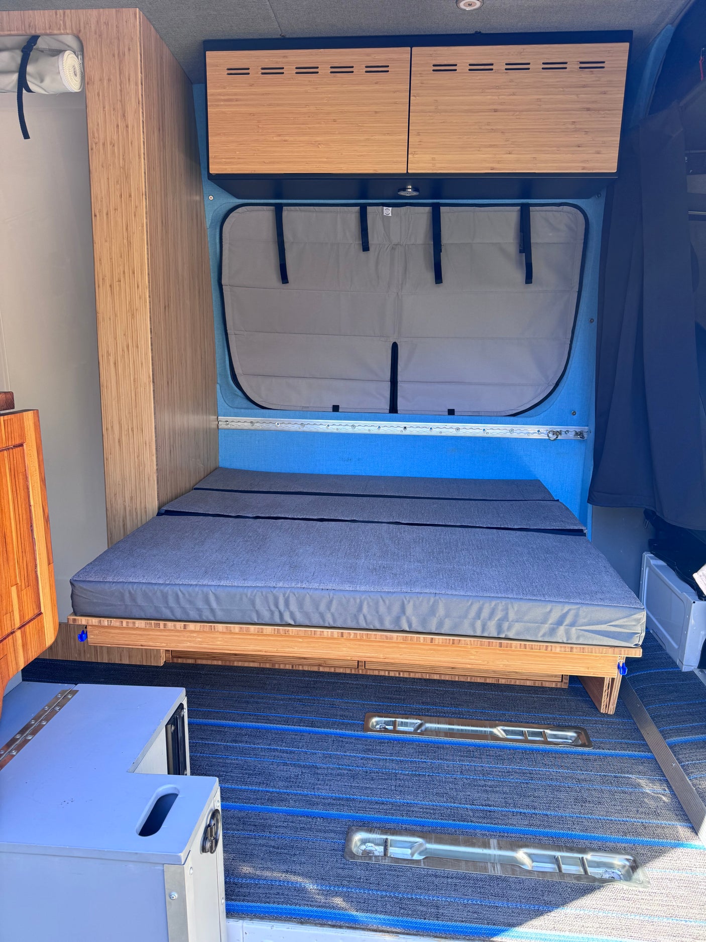 Ready for adventure? This RV rental offers a compact camper van interior with a bed, wood cabinets, and blue accents.