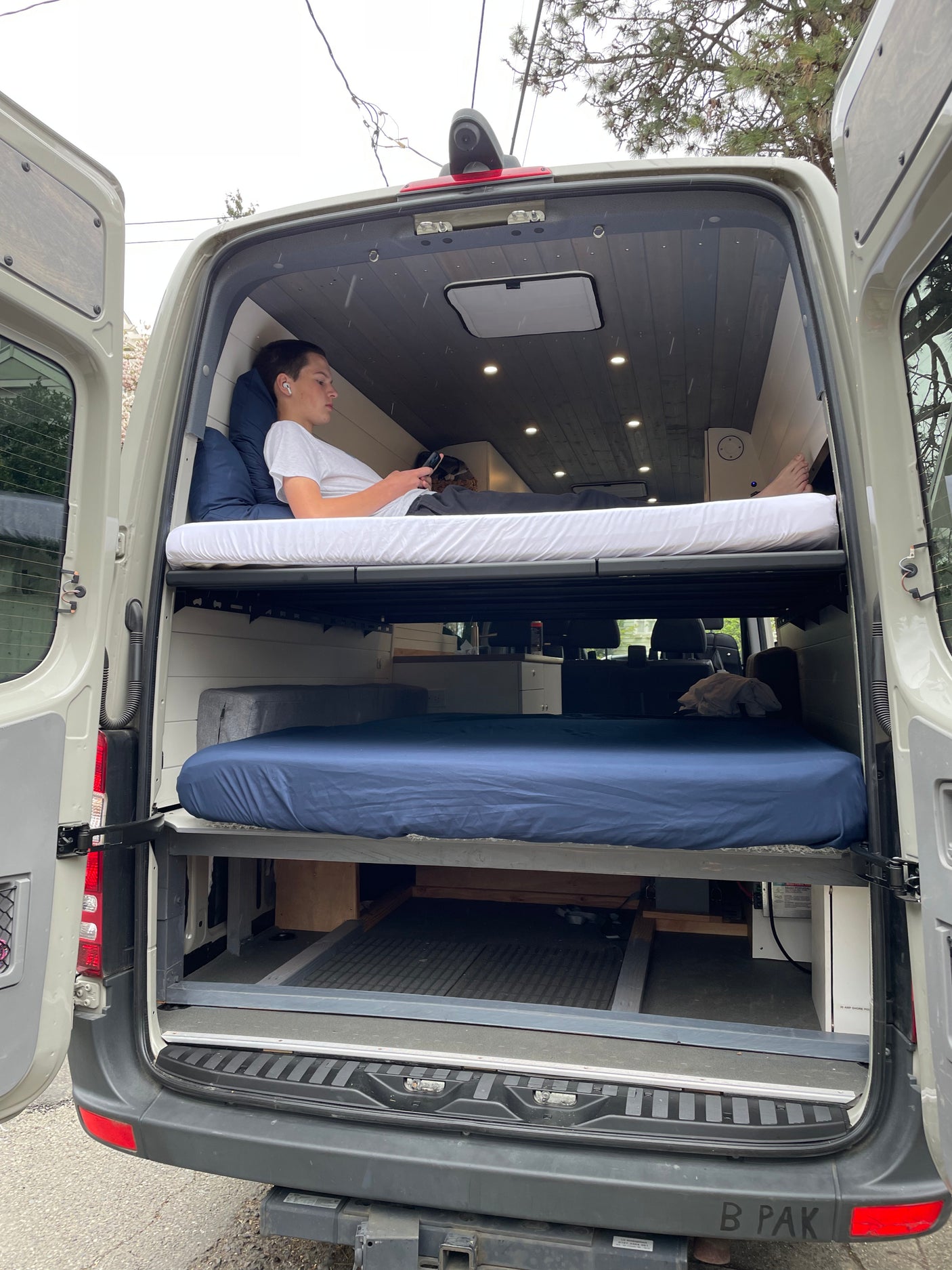 Inside an RV rental, this camper van features bunk beds for mobile living. A person relaxes on the top bunk, ideal for travel.